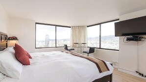 A hotel room with a large bed, a TV mounted on the wall, and a city view through large windows. - Renovated Specious Studio with Great View (Honolulu)