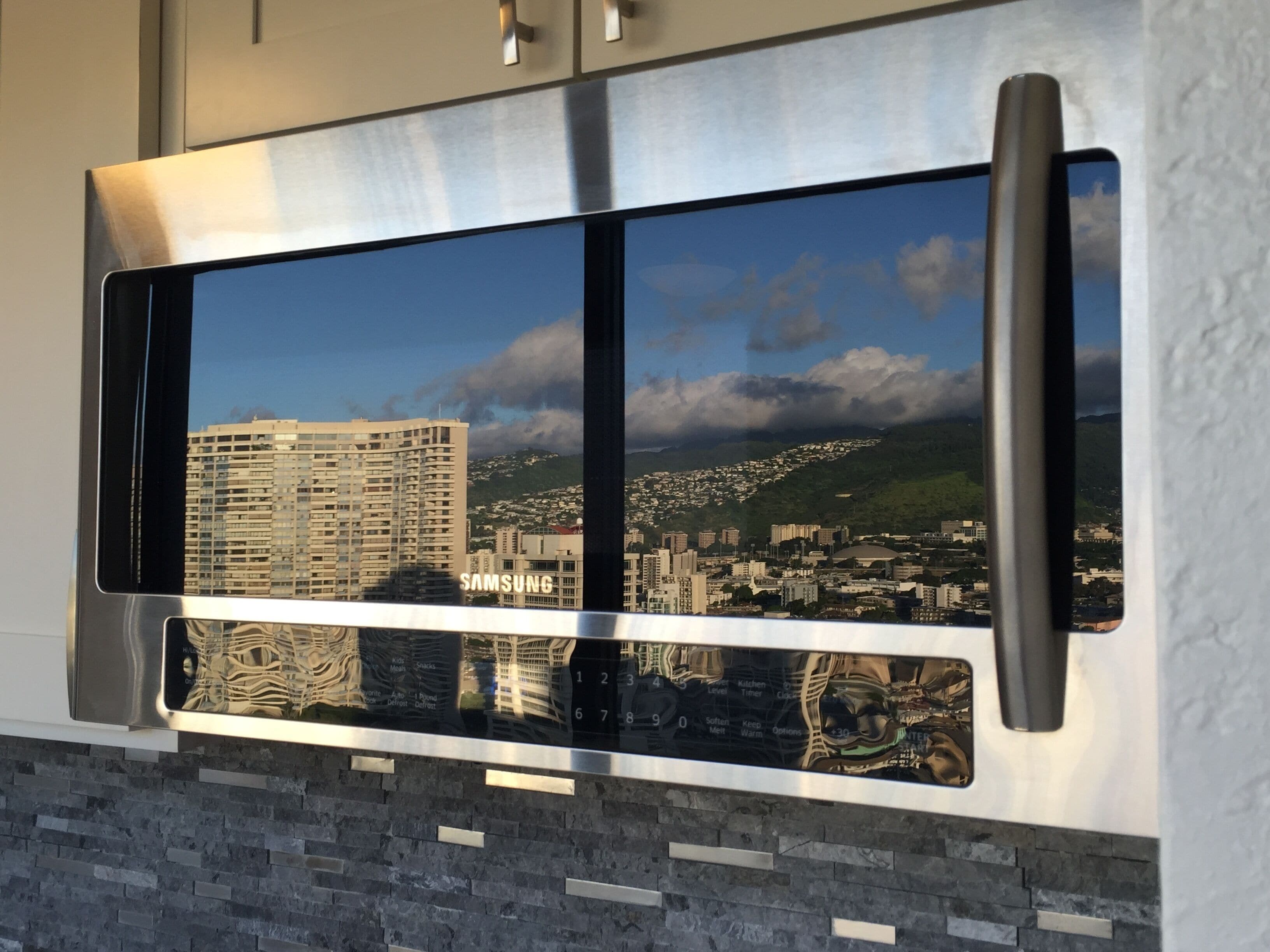 Une cuisine moderne dotée d’une hotte en acier inoxydable et d’une grande fenêtre offrant une vue sur le paysage urbain.