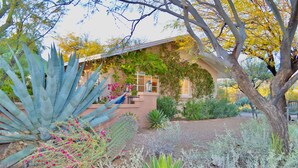 Una casa con patio techado, rodeada de diversas plantas del desierto y una gran planta de agave.