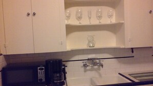 Una cocina con gabinetes blancos, cafetera, jarra de vidrio y un lavamanos.