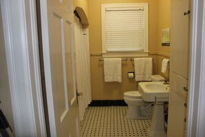A bathroom with a toilet, sink, and window. There are towels hanging on a rack.