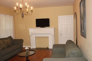 A living room with two sofas, a fireplace, a television, and a chandelier.