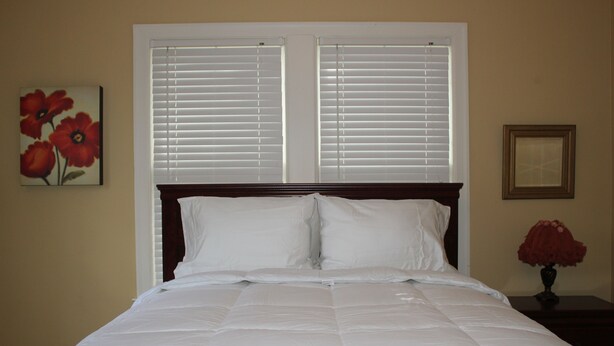 Una cama bien hecha con ropa blanca, cabecera de madera y ventana con persianas.