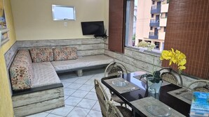 A living room with a sofa, a dining table, and a TV mounted on the wall. - Apartamentos Adriático Guarujá (Guarujá)