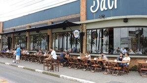 An outdoor cafe with wooden tables and chairs, a blue awning, and a sign reading "Datti". - Apartamentos Adriático Guarujá (Guarujá)