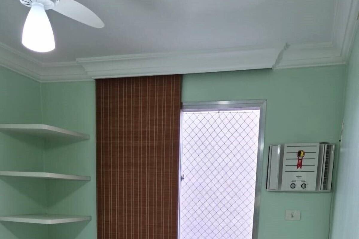 Een slaapkamer met een bed, een plafondventilator, een raam met jaloezieën, een radiator en een betegelde vloer.