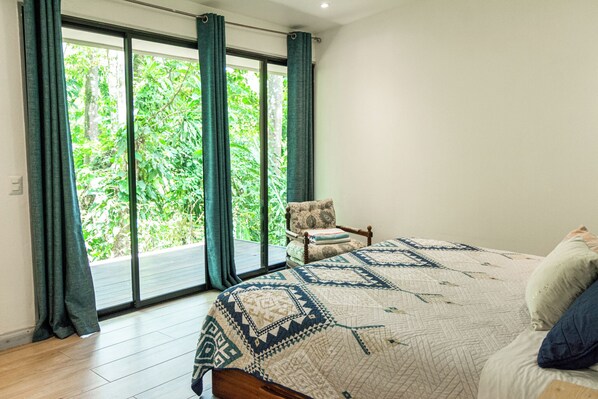 A bedroom with a large bed, a chair, and a view of greenery through a sliding door. - Selva Color Forest & Beach Ecolodge (Tárcoles)