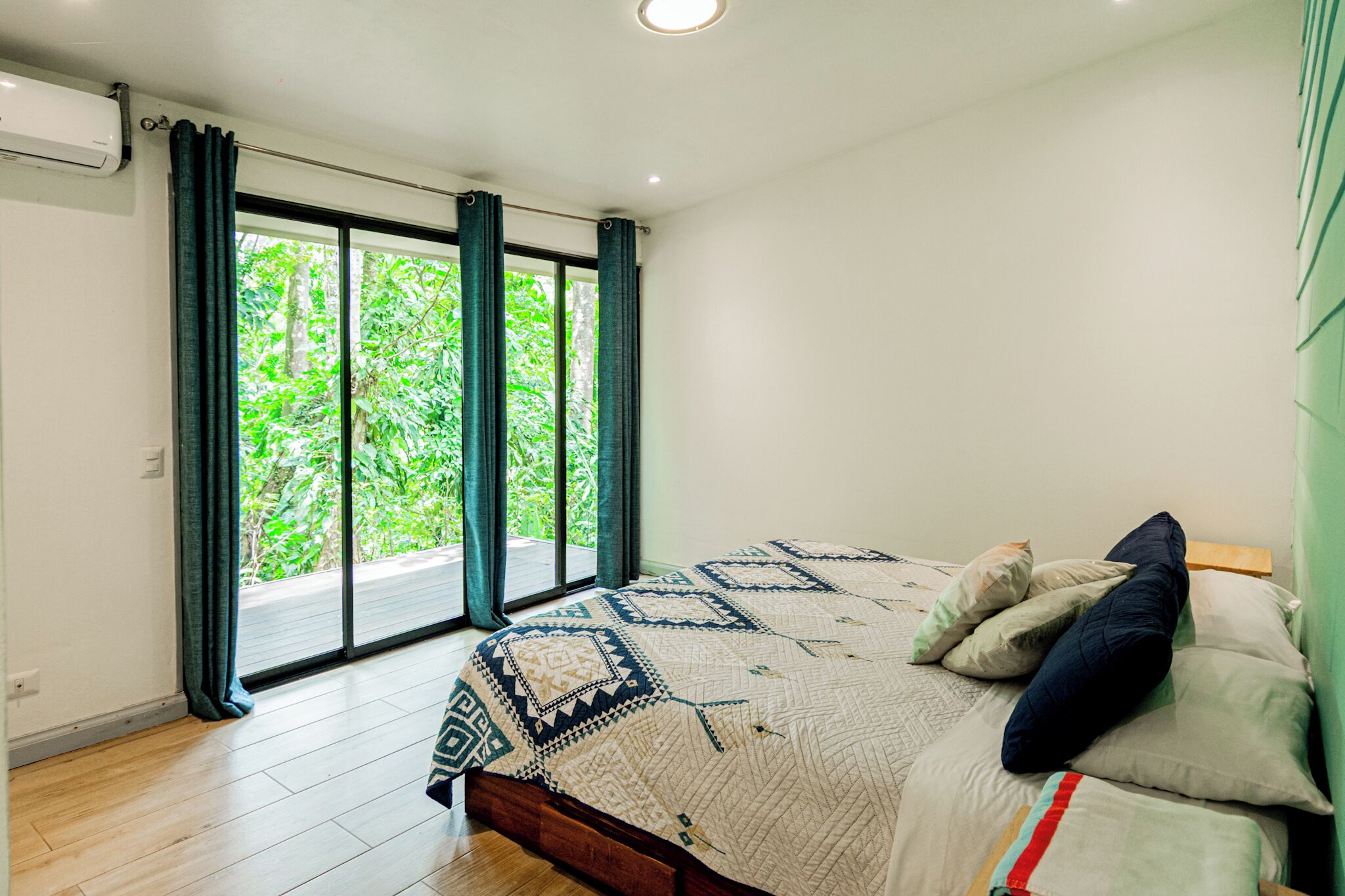 Ein Schlafzimmer mit einem großen Bett, Blick durch eine Schiebetür auf einen Balkon und einem Deckenventilator.