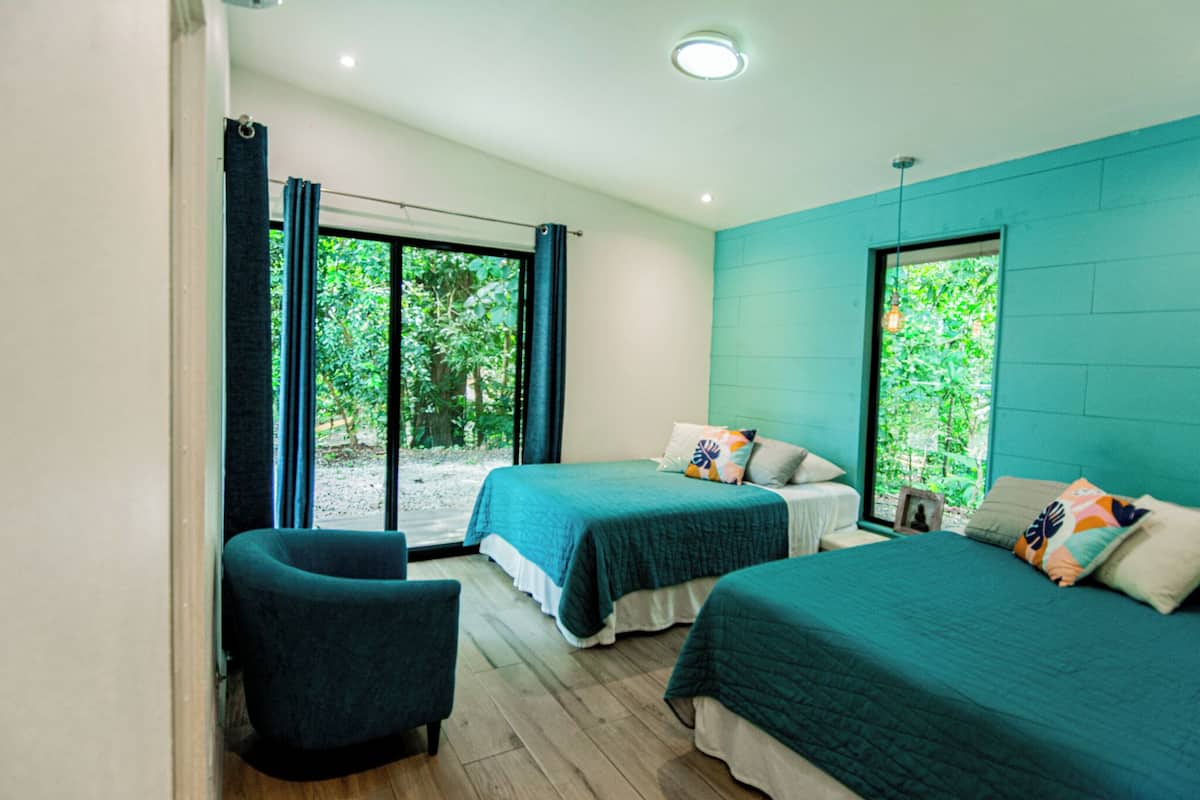 A modern bedroom with two beds, a chair, and large windows.