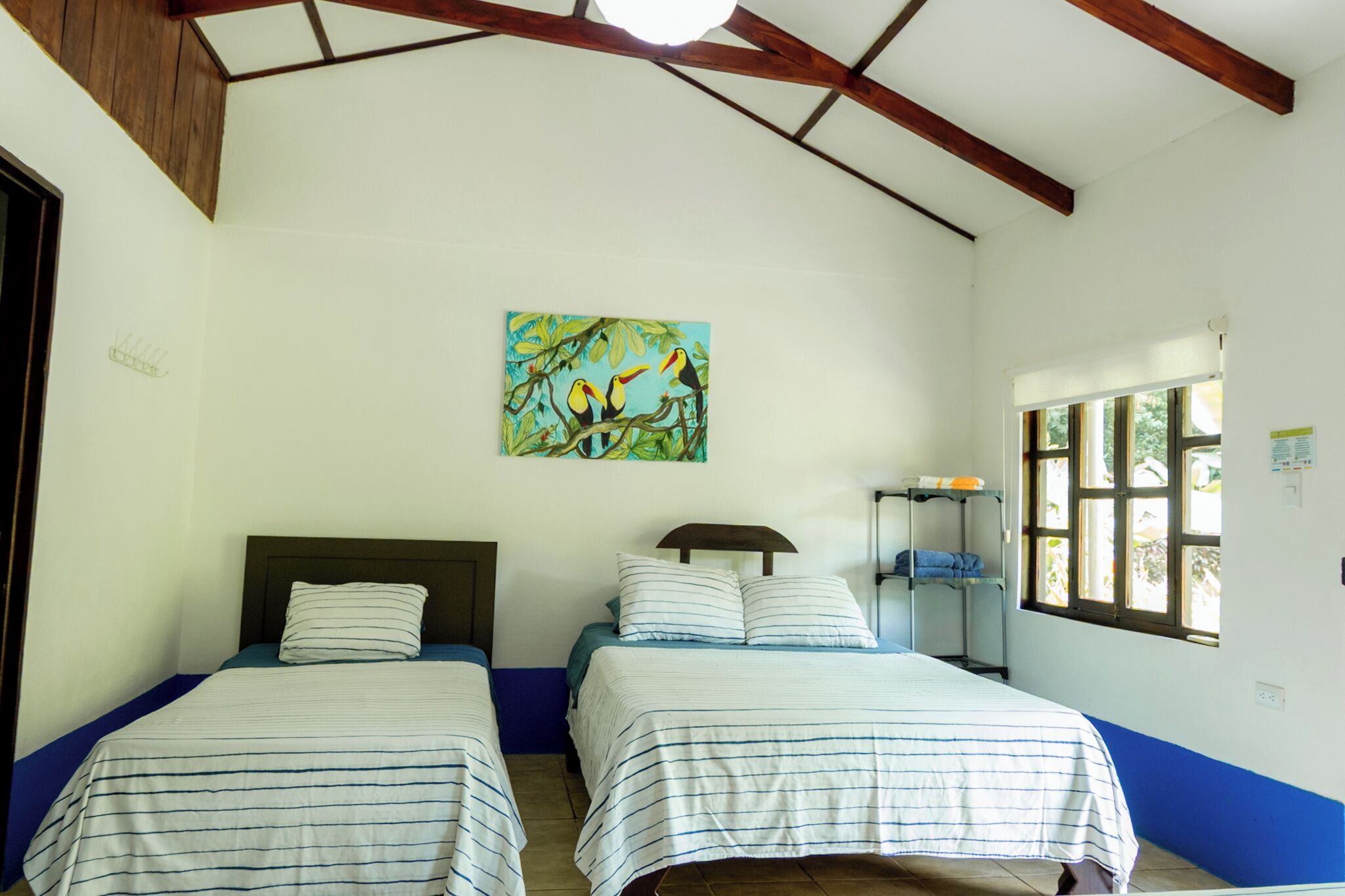 Quarto com duas camas, um quadro na parede e janela com vista.
