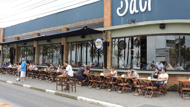 A restaurant with outdoor seating and a large sign. - Apartamento Baia Blanca Guarujá (Guarujá)