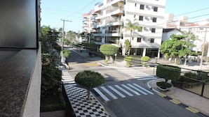 A street view with a checkered pavement, a pedestrian crossing, and a multi-story building with balconies. - Apartamento Lester Primo Guarujá (Guarujá)