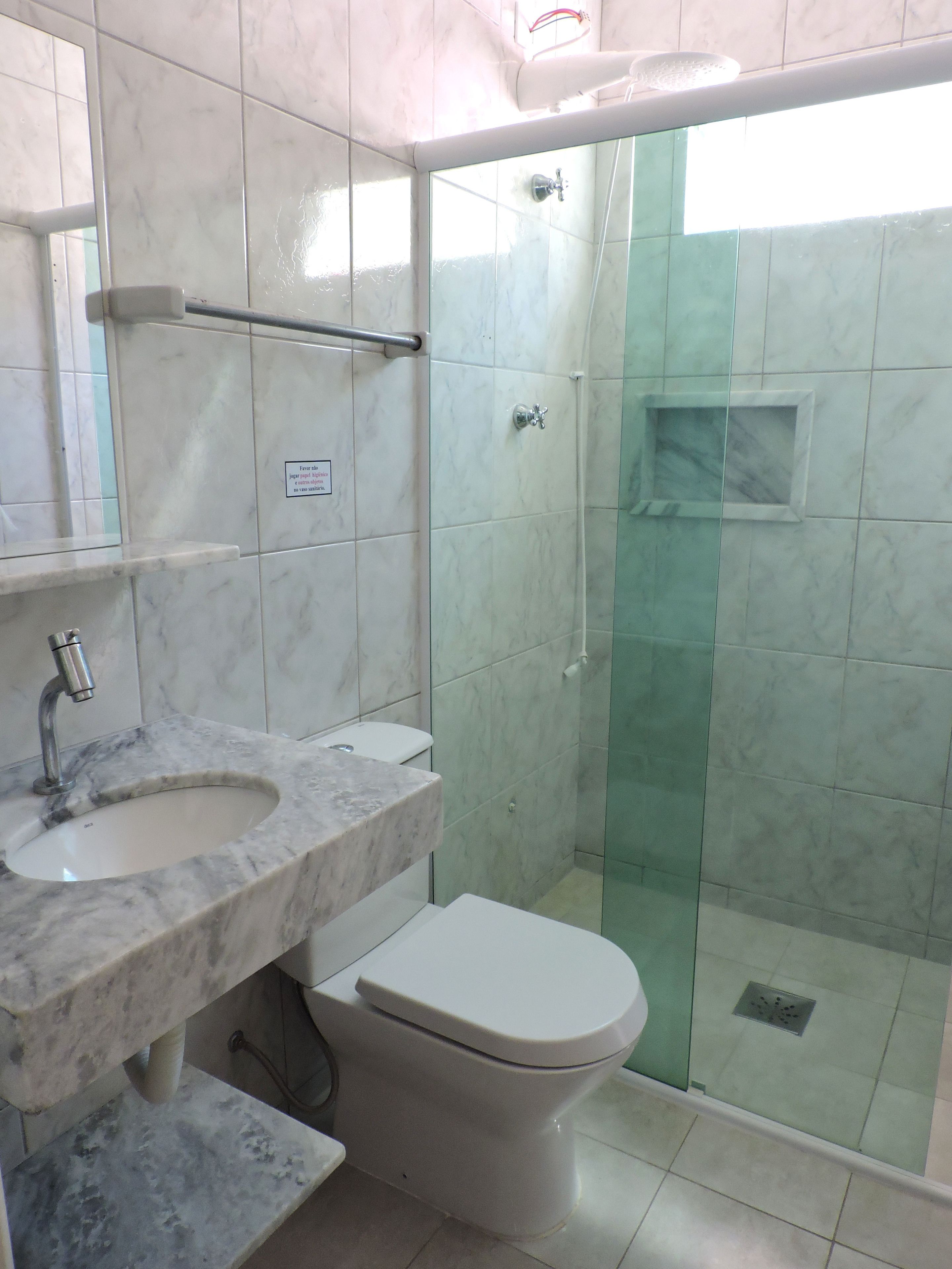 Un baño con lavamanos de mármol, inodoro y ducha con mampara de vidrio.