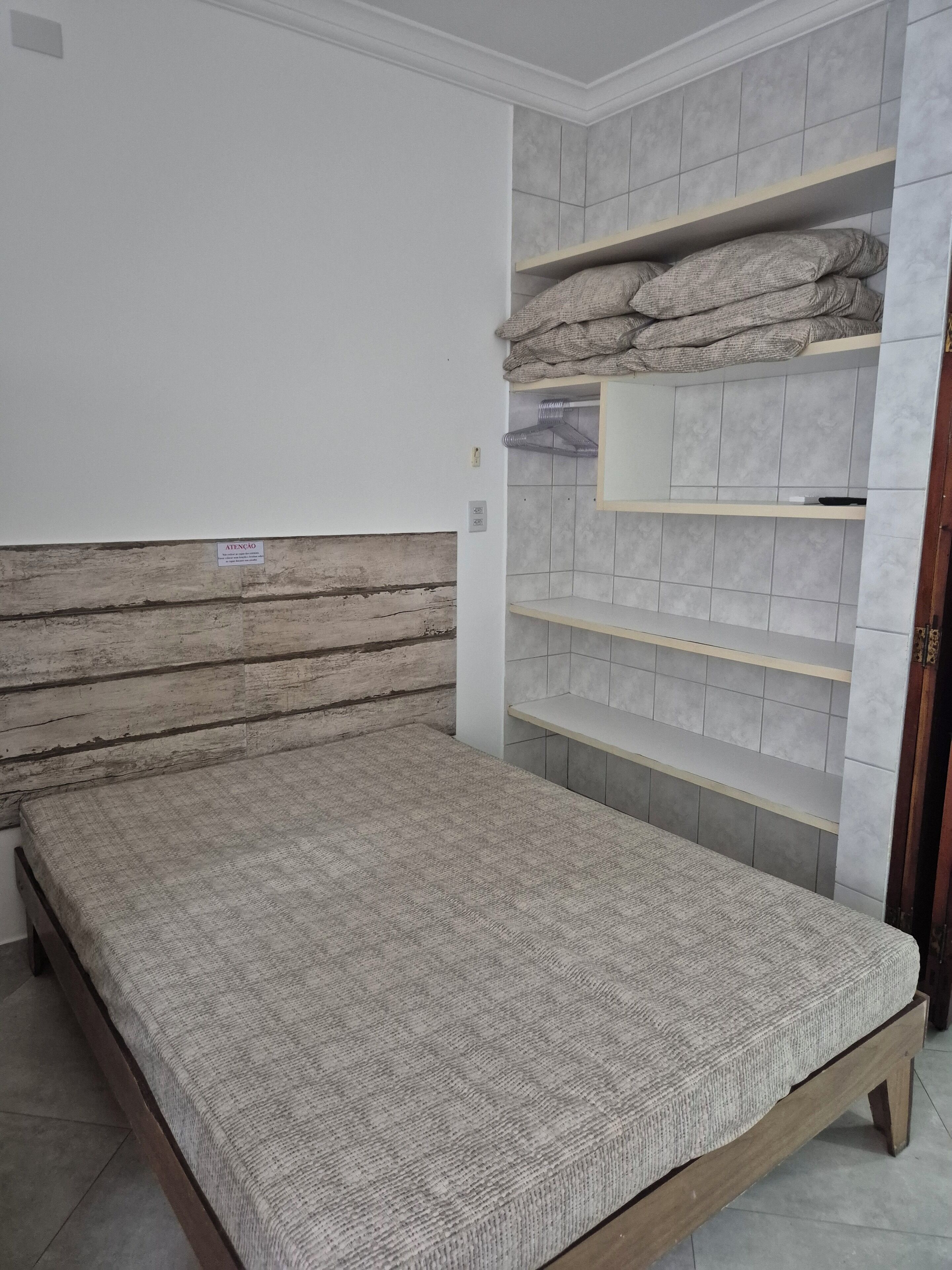 A bedroom with a wooden headboard, a bed with a grey textured mattress, and built-in shelving with storage space.