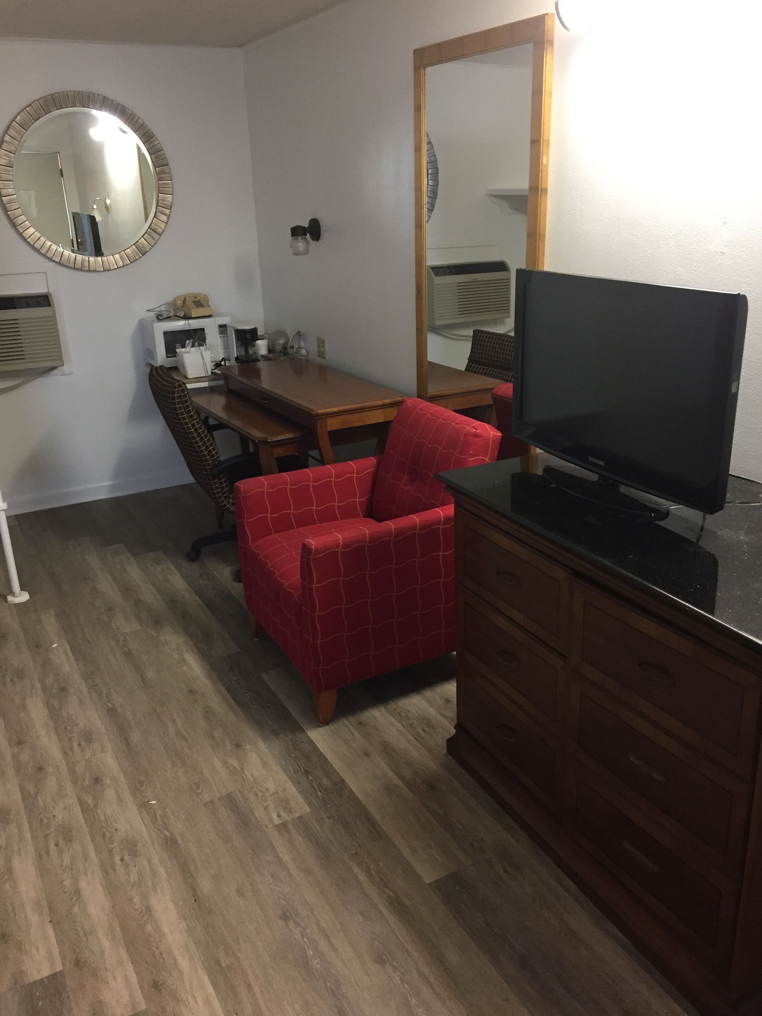 A compact room with a wooden desk, a red chair, a television, a mirror, and a microwave.
