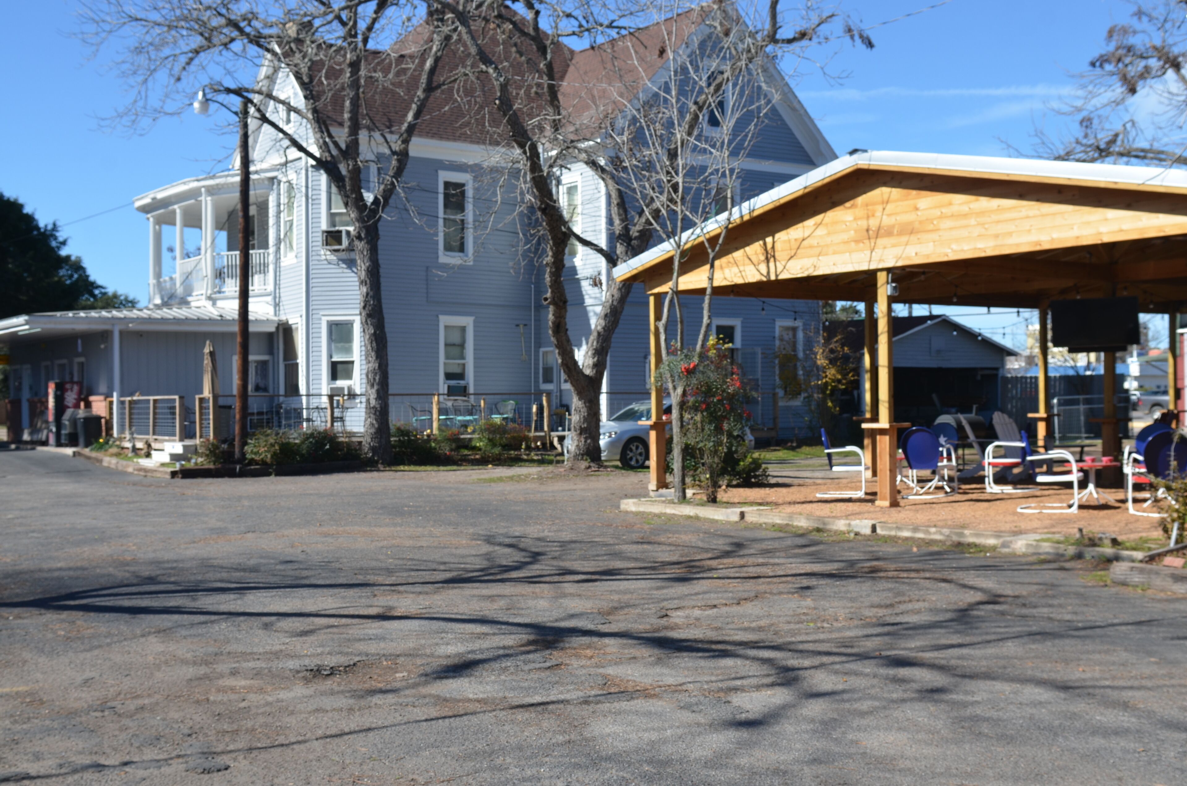 A parking lot with a covered seating area and a large house in the background.
