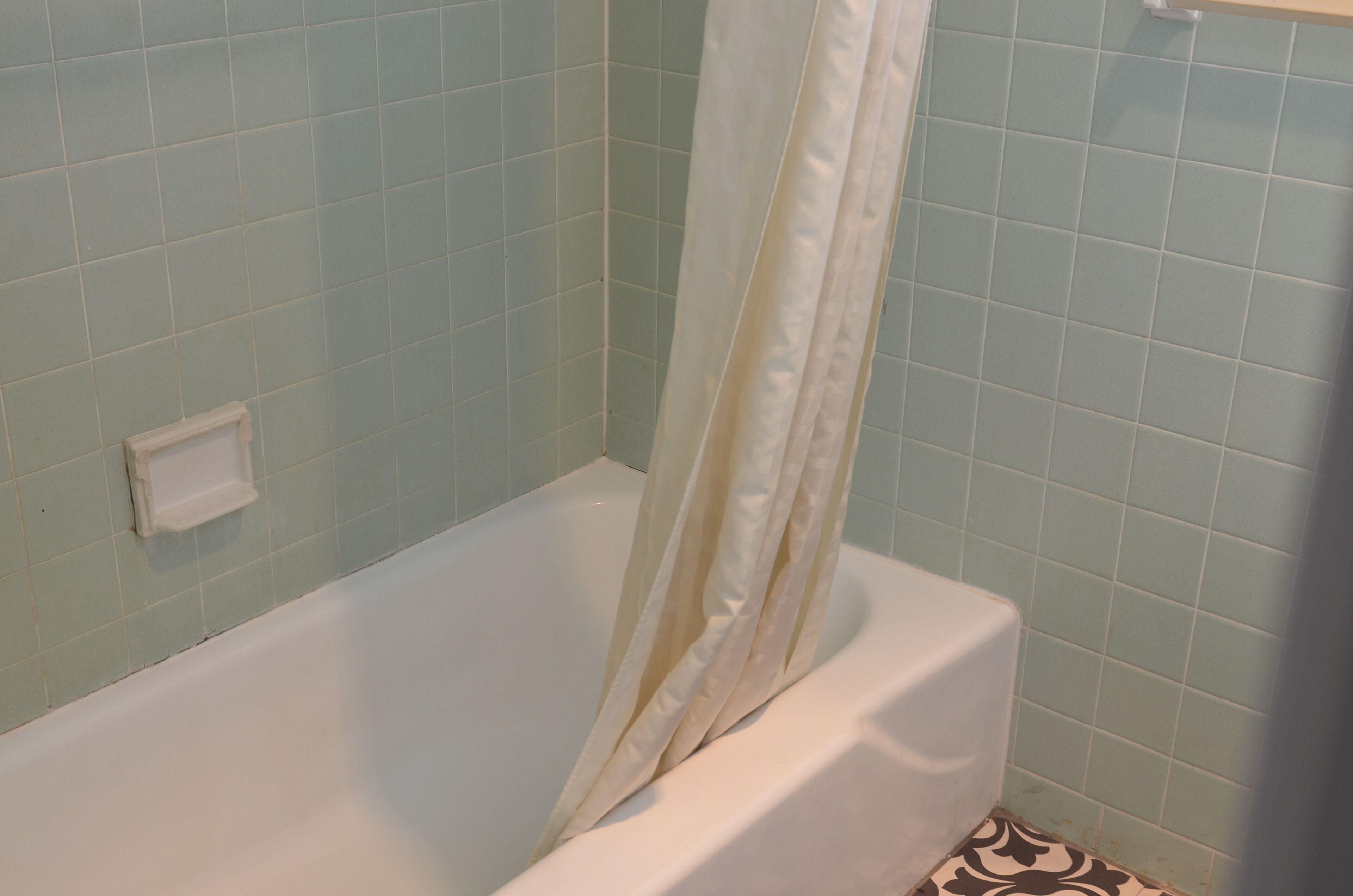 Una bañera con cortina de ducha en un baño con paredes de azulejos azul claro.