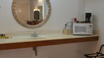 A bathroom with a round mirror, a sink, a coffee maker, and toiletries on the counter.
