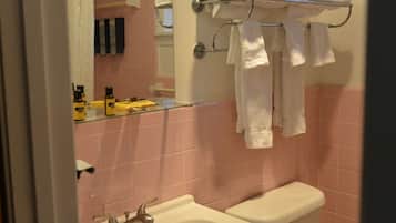 A bathroom with pink tiles, a glass shower enclosure, a white sink, and a toilet. There are towels hanging on a rack above the toilet.