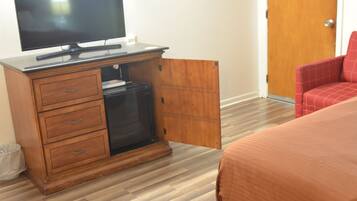 A hotel room with a wooden cabinet, a television, a red chair, and a bed with a brown bedspread.