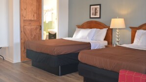 Una camera d'albergo con due letti, una porta in legno, una lampada e un quadro appeso al muro.