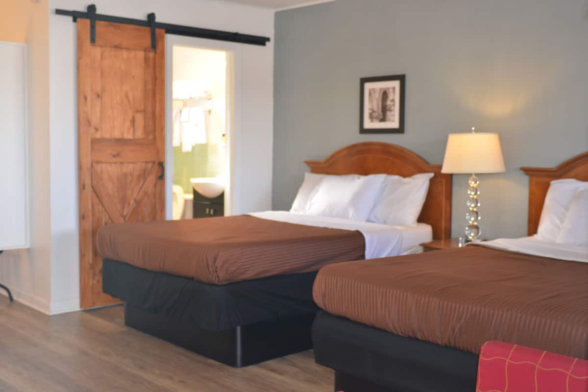 Una habitación de hotel con dos camas, una puerta de madera, una lámpara y un cuadro en la pared.