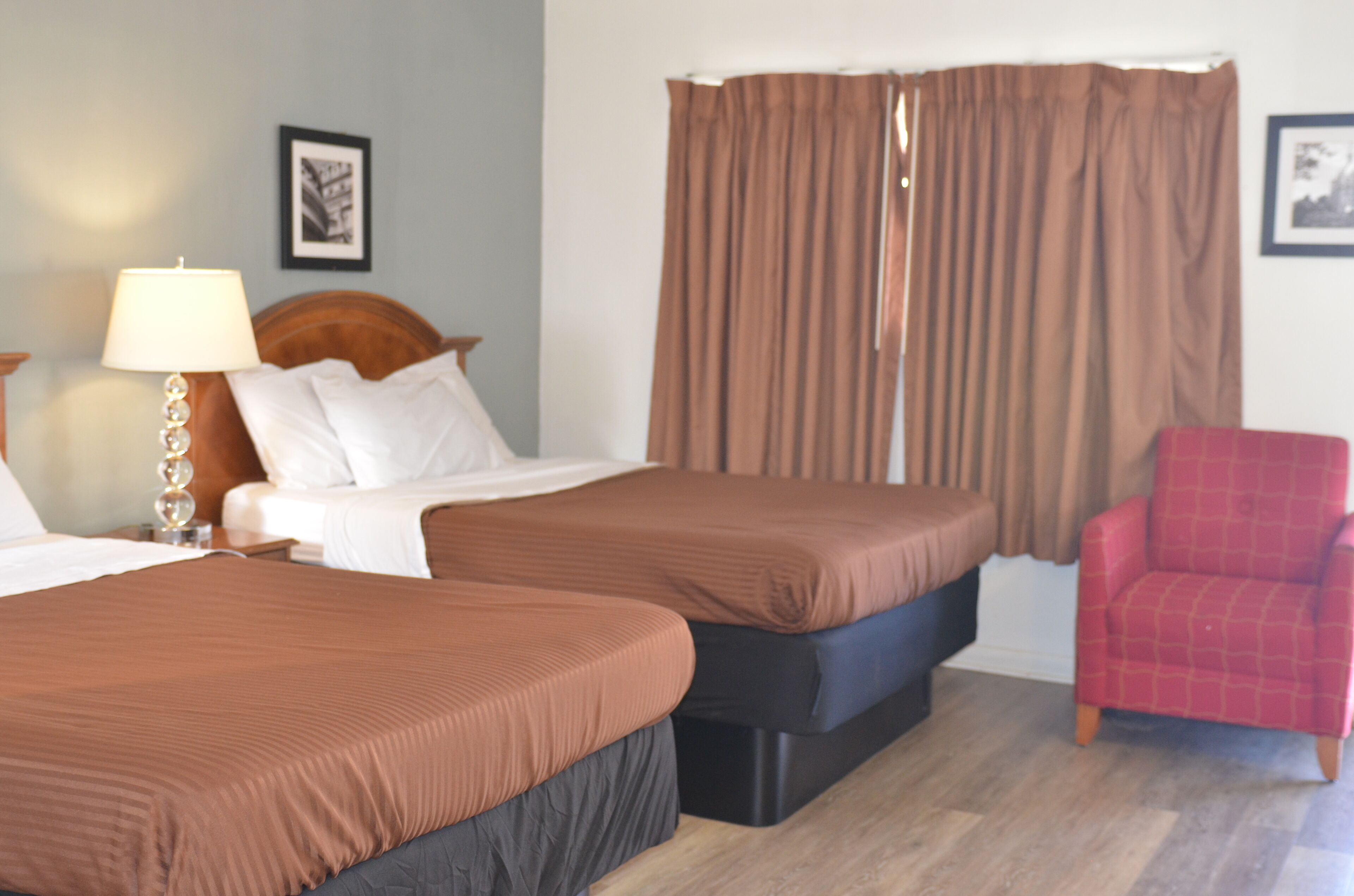 Una habitación de hotel con dos camas, un sillón rojo, una lámpara y cortinas.