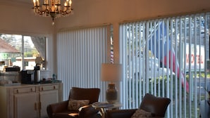 Una camera d'hotel con zona pranzo, due poltrone in pelle, un tavolo con una lampada e vista all'esterno attraverso ampie finestre.