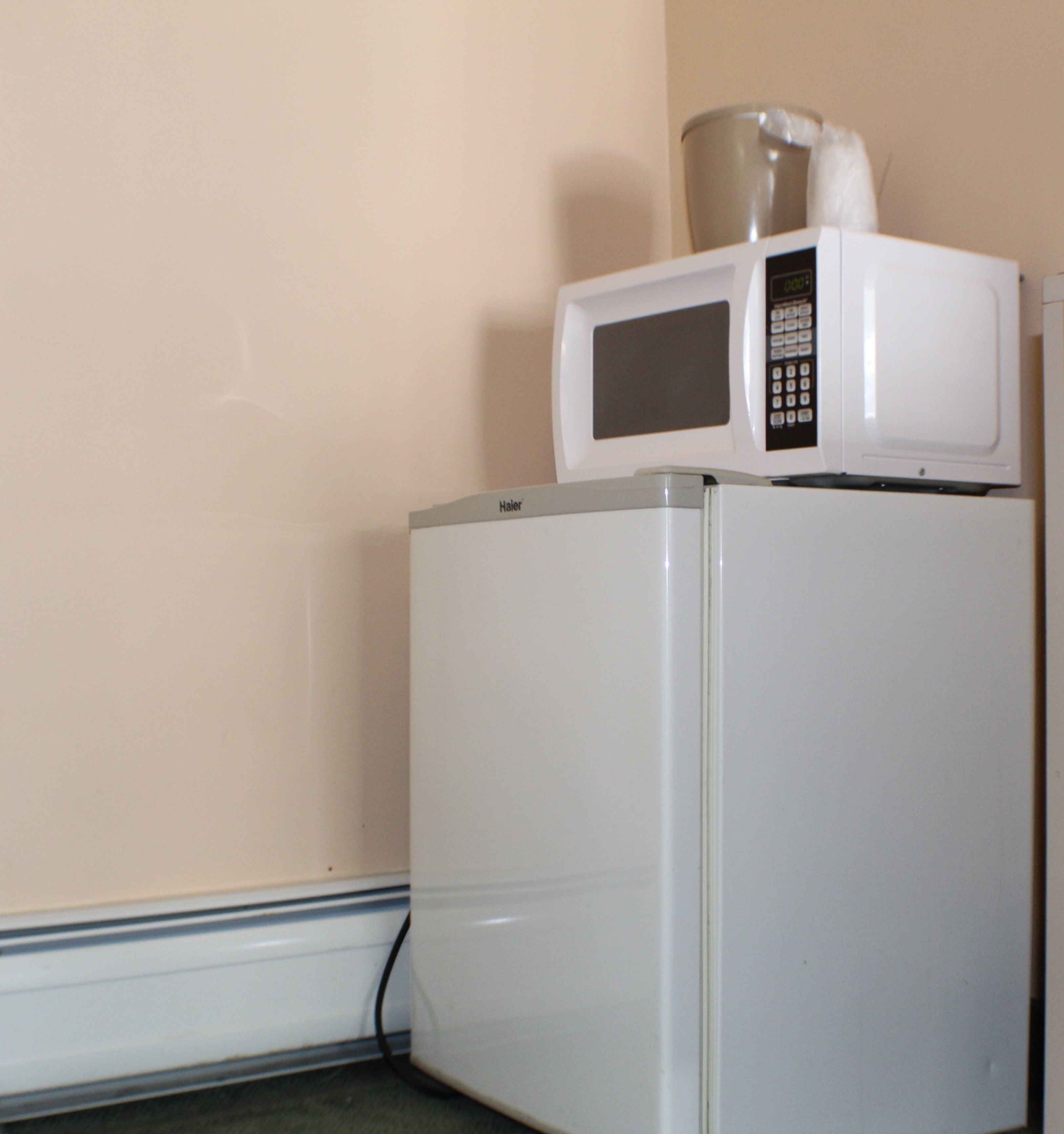 A white refrigerator with a microwave on top, placed against a plain wall.
