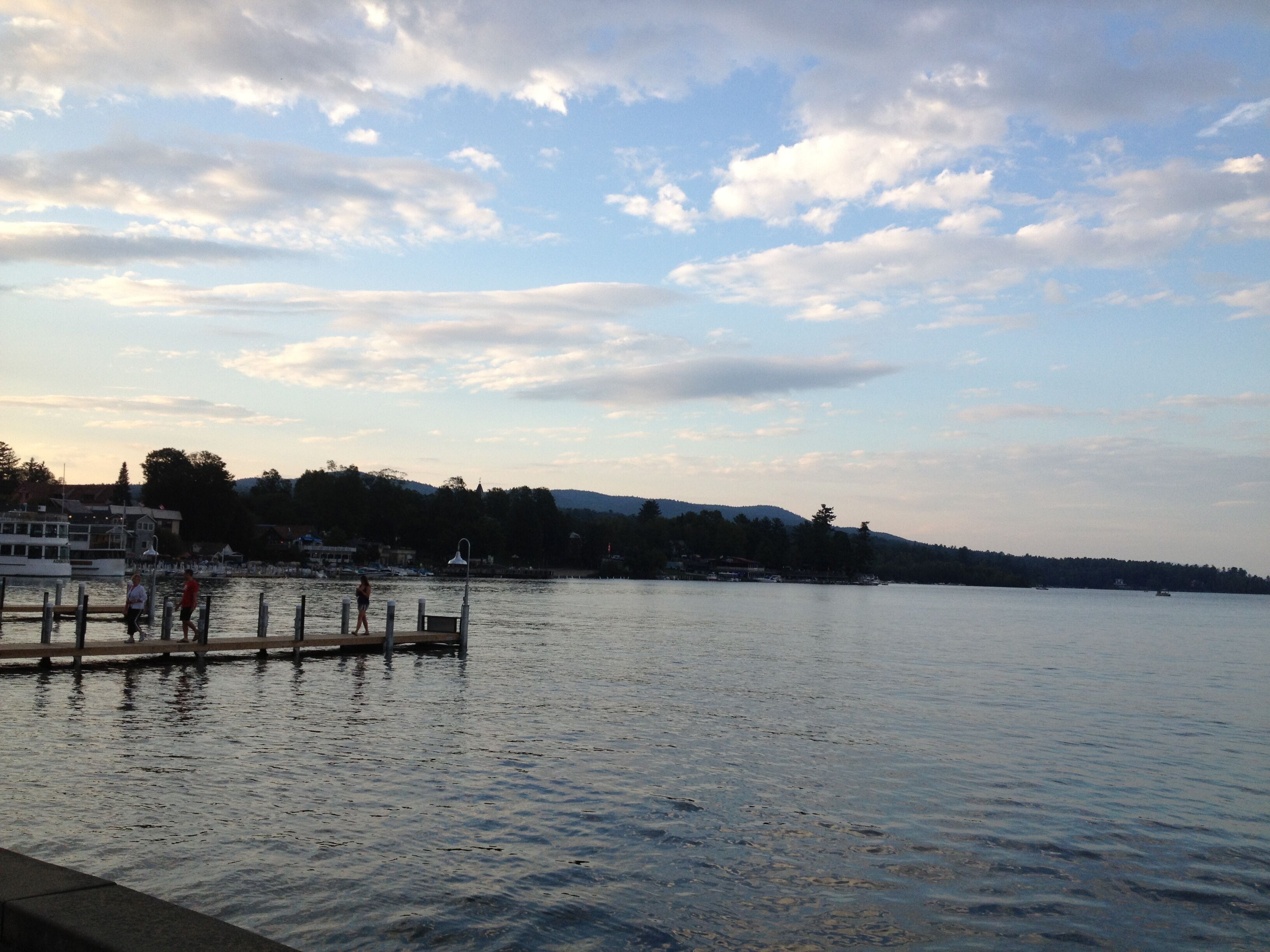 A waterfront view with a dock, calm water, and a distant shoreline with buildings and trees.