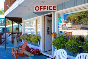 An office building with a sign reading "OFFICE" above the entrance. There are potted plants and flowers outside, and a wooden chair is visible on the porch. - Lake Haven Motel (Lake George)