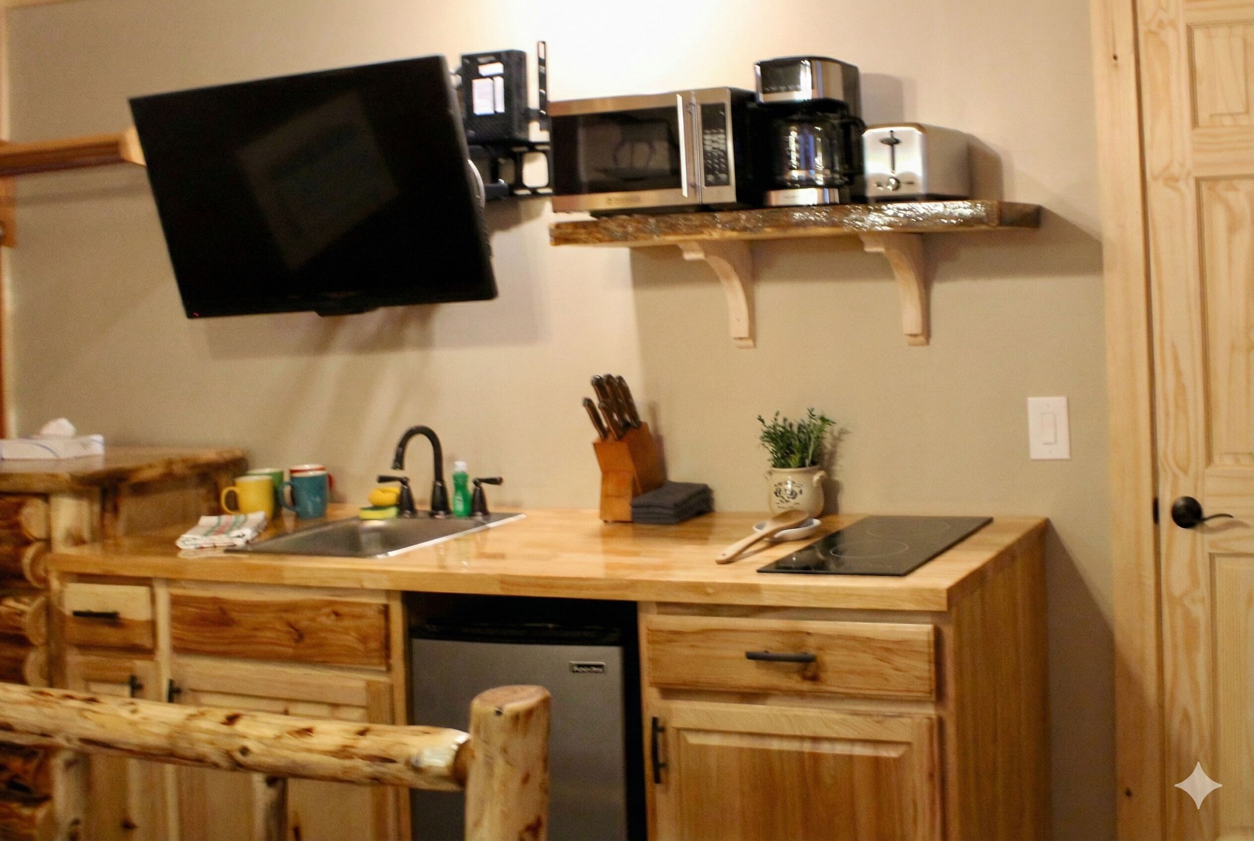 Una cocina compacta con lavavajillas integrado, armarios de madera, microondas, tostadora y un televisor de pantalla plana montado en la pared.