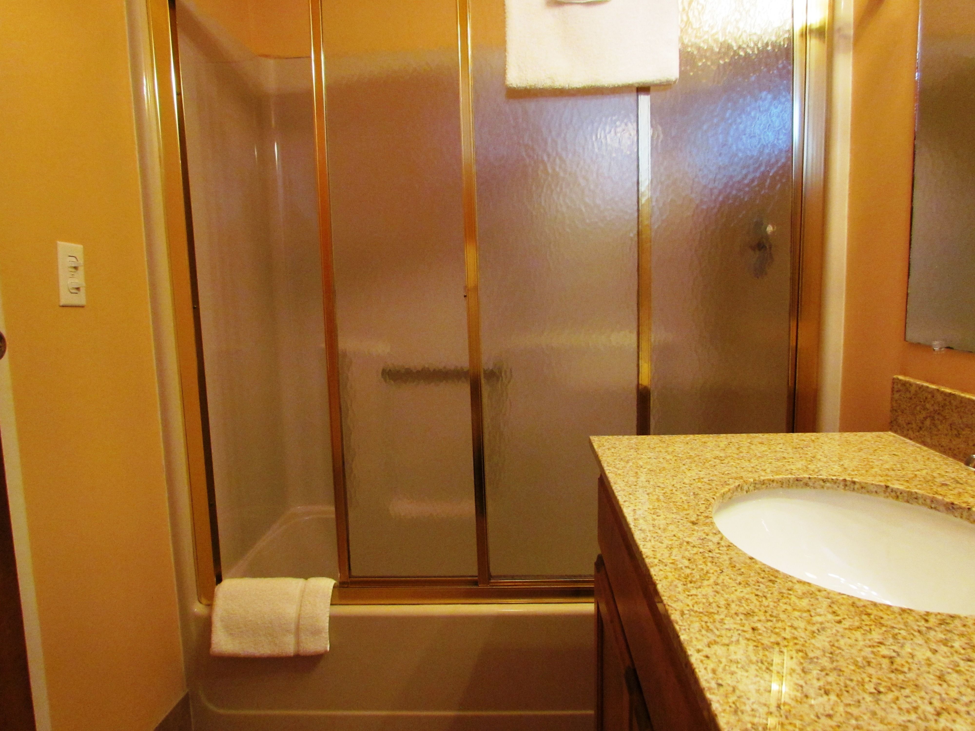 A bathroom with a glass-enclosed shower, a sink with a granite countertop, and a towel hanging on the wall.
