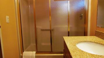 A bathroom with a glass-enclosed shower, a sink with a granite countertop, and a towel hanging on the wall.