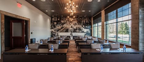 Une salle de conférence équipée de tables et de chaises, d’un lustre et de grandes fenêtres.