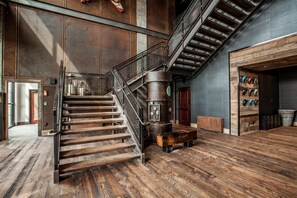Un hall d’entrée spacieux avec un escalier en bois, un grand radiateur de style industriel et un mur où sont exposés différents chapeaux.