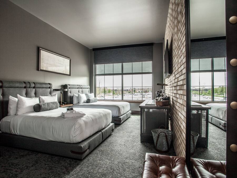 A modern hotel room with a large bed, two smaller beds, a seating area, and a view of the city.
