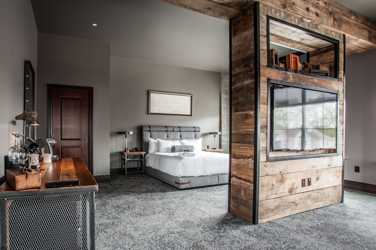 Ein modernes Schlafzimmer mit einem großen Bett, einer Wandpaneele aus Holz, einem eingebauten Fernseher und einem Schreibtisch mit Spiegel.