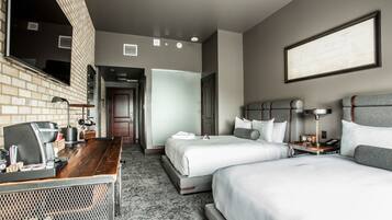 A hotel room with two beds, a desk with a coffee machine, a TV, and a framed picture on the wall.