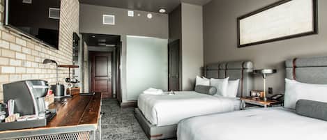 A hotel room with two beds, a desk with a coffee machine, a TV, and a framed picture on the wall.