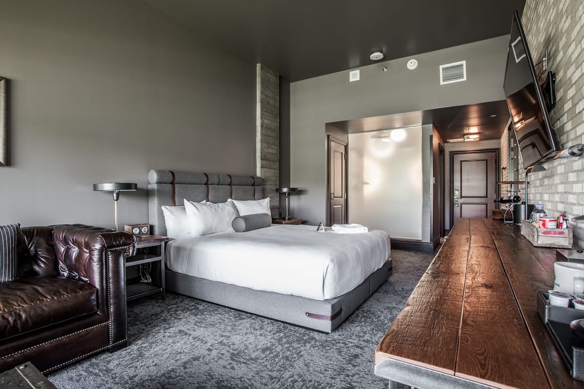 Ein modernes Hotelzimmer mit einem großen Bett, einem Ledersofa, einem Holzesstisch und einer Küchenzeile.