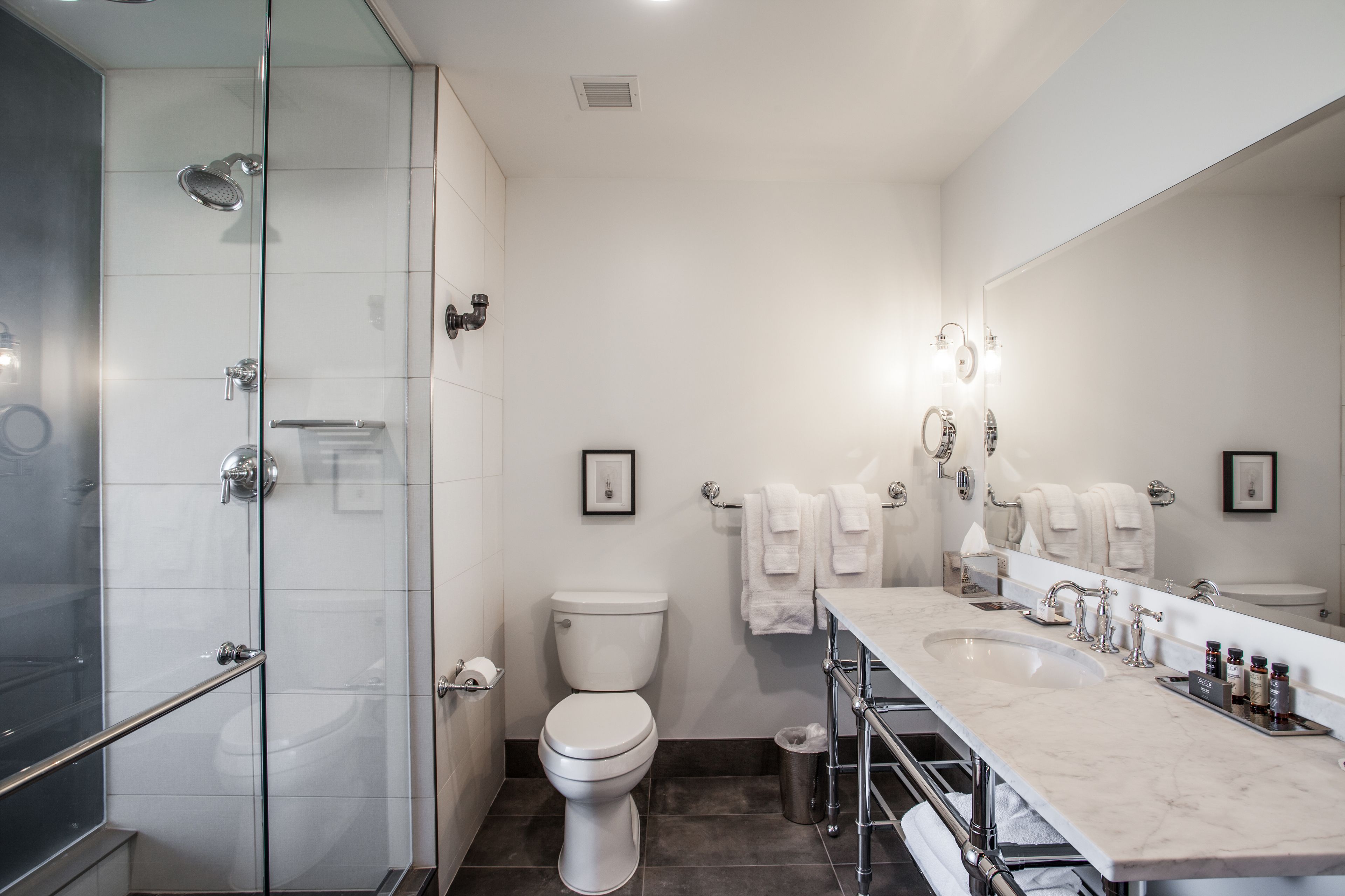 A modern bathroom with a glass shower enclosure, a white toilet, a large vanity with a mirror, and multiple towels.