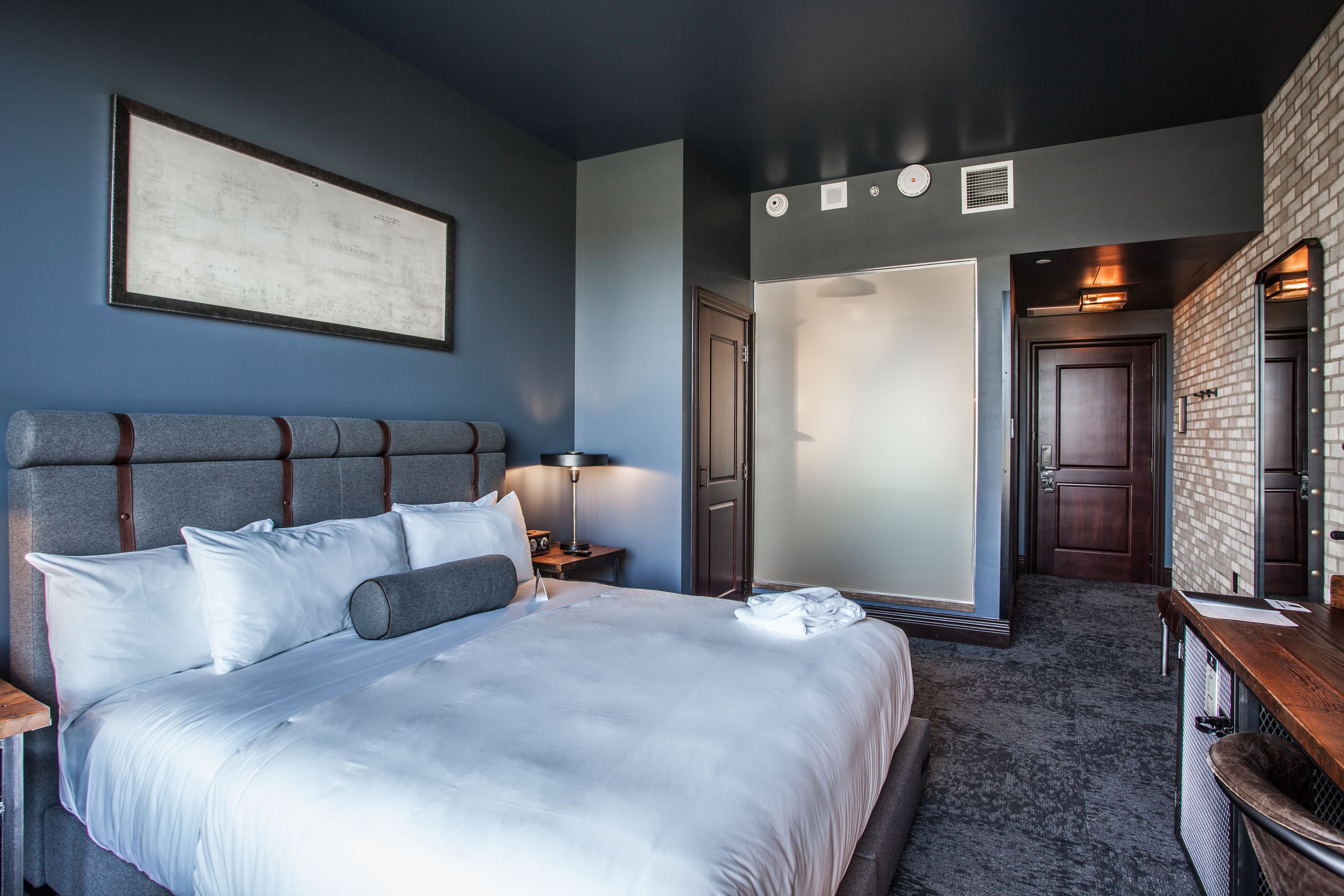 Una habitación de hotel con una cama grande, una mesita de noche, un escritorio y un espejo.