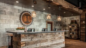 A rustic reception desk with a wooden finish, a metal mesh wall, and pendant lighting. - Ironworks Hotel Indy (Indianapolis)