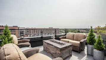 A rooftop patio with wicker furniture, a stone fire pit, and potted Christmas trees.