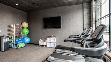 A gym with treadmills, exercise balls, and a TV on the wall.