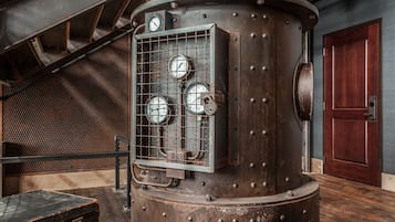 A large industrial-style boiler with gauges, a wooden bench, and a wooden door in the background.