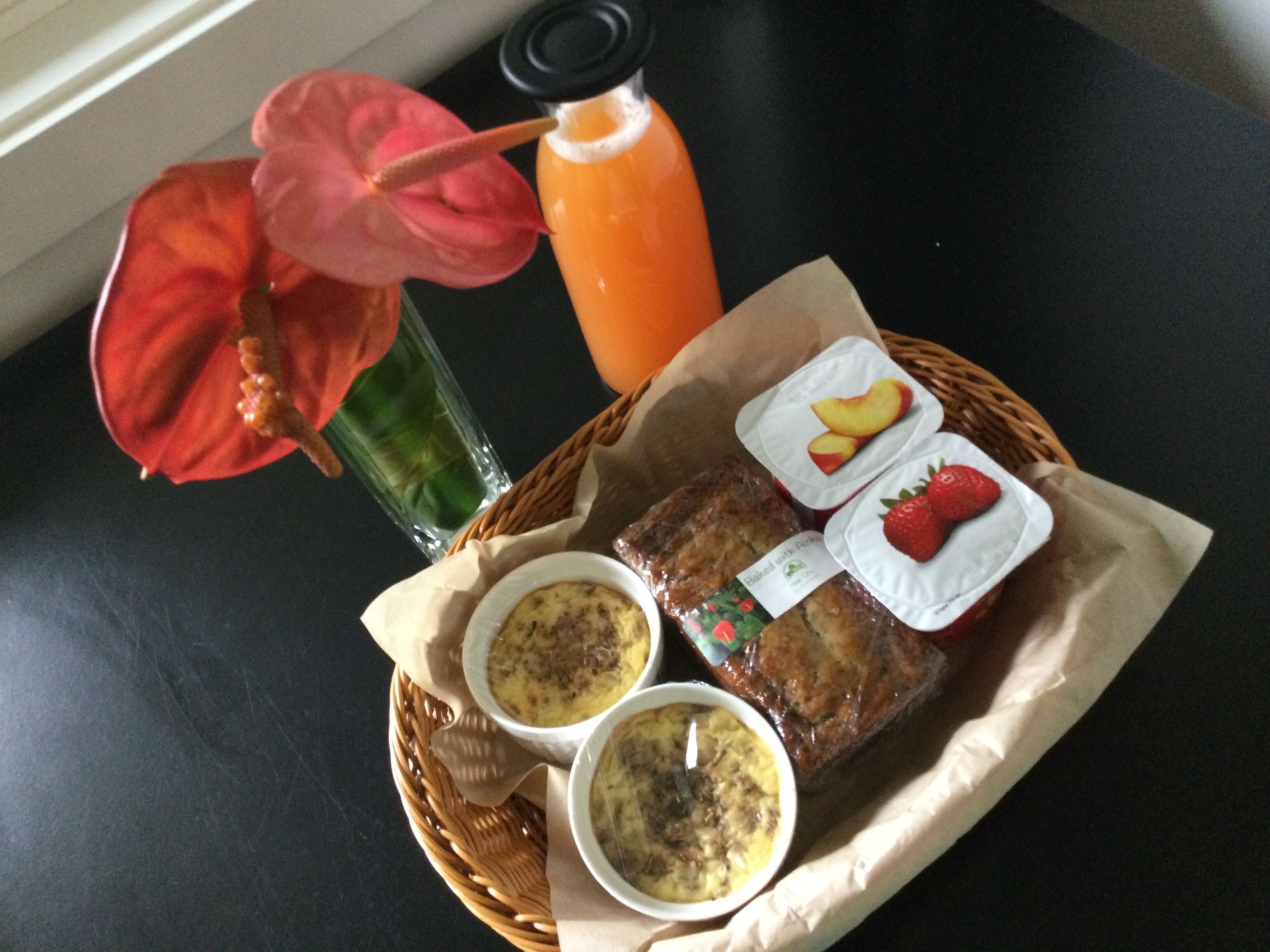 A meal with a bottle of orange juice, two containers of food, and a red flower.