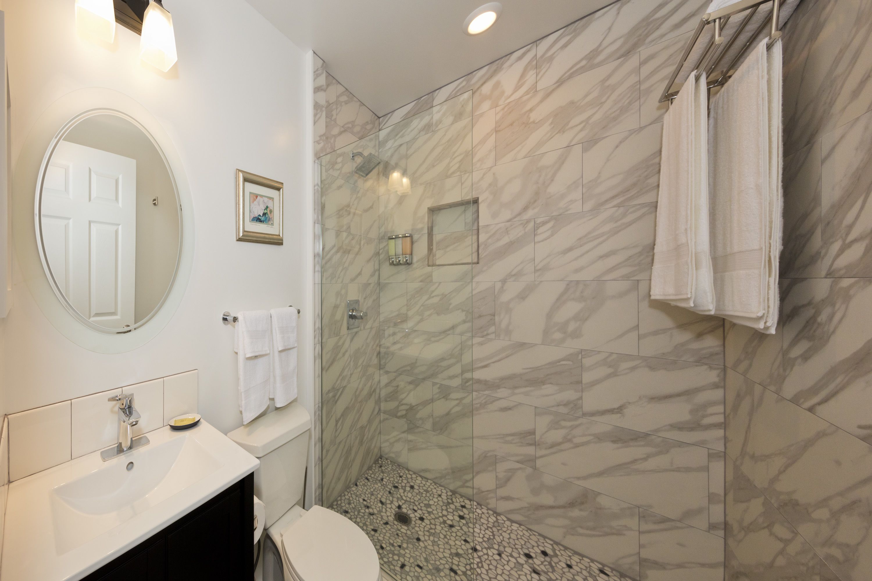 Un baño con ducha de mármol, lavamanos e inodoro.