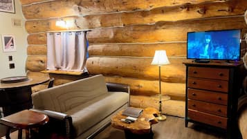 Interior acogedor de una cabaña de troncos con un sofá, una mesa de centro de madera, un televisor y una lámpara.